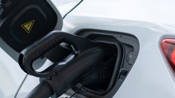 Ein weißes Auto tankt an einer Tankstelle. Der Kraftstoffschlauch ist in die Tanköffnung gesteckt, während der Tankdeckel geöffnet ist. Das Bild zeigt den Tankvorgang eines Fahrzeugs.