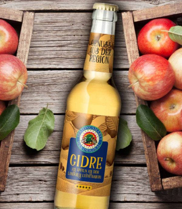Das Bild zeigt eine Flasche Cidre mit der Aufschrift "GIDRE" in der Mitte. Um die Flasche herum liegen frische Äpfel und einige Blätter. Der Hintergrund besteht aus Holzbrettern, die eine rustikale Atmosphäre schaffen.