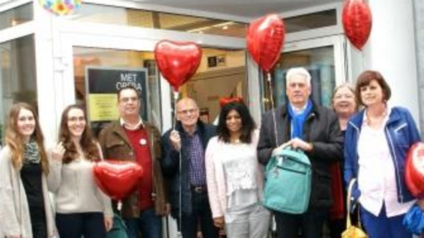 A group of seven people stands outside the Central Theater, smiling. They hold red heart-shaped balloons and a light blue backpack. The atmosphere is festive, suggesting a celebration or event taking place at the theater.