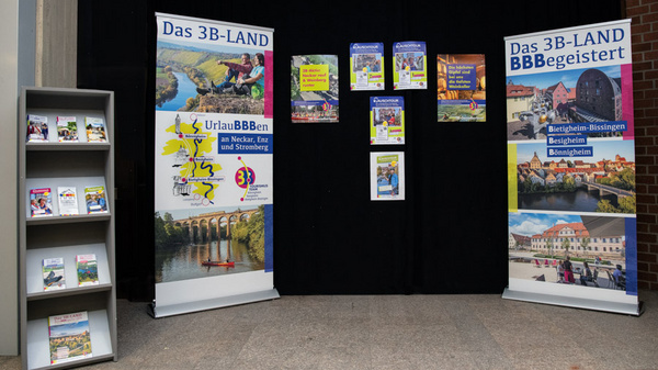 Das Bild zeigt einen Informationsstand für das 3B-LAND mit zwei großen Rollups. Diese präsentieren touristische Ziele und Aktivitäten in Bietigheim-Bissingen, Bönnigheim und Erligheim. Neben den Rollups steht ein Regal mit Broschüren zu den Angeboten der Region.