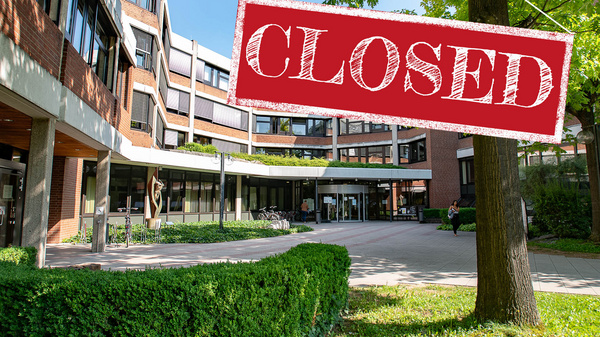 Un bâtiment moderne est visible, avec une entrée spacieuse et des espaces verts alentour. Un panneau rouge suspendu indique "CLOSED" (fermé), signalant que l'établissement n'est pas ouvert au public. (Text KI generiert)