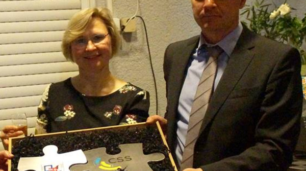 Tre persone in abiti formali sorreggono un grande pezzo di puzzle che presenta il logo di CSS. Sono visibilmente sorridenti e festosi, dando l'idea di un momento di celebrazione o di un evento significativo.