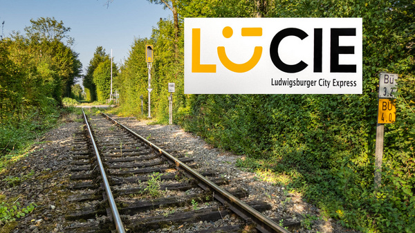 Das Bild zeigt eine ruhige, von Bäumen gesäumte Bahngleisstrecke. Im Vordergrund sind die Gleise sichtbar, die ins Grün führen. Oben rechts befindet sich das Logo "LÜ CIE", das für den Ludwigsburger City Express steht.