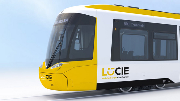 Ein moderner Straßenbahnwagen mit einer gelben und weißen Farbgestaltung. Die Vorderseite zeigt eine große Windschutzscheibe, während auf der Seite das Logo „LUCIE“ und ein Symbol für Barrierefreiheit zu sehen sind. Die Bahn steht auf einem Schienennetz vor einem hellen, nebligen Hintergrund.