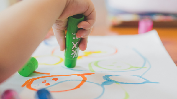 Ein Kind hält einen grünen Marker und malt auf ein weißes Blatt Papier