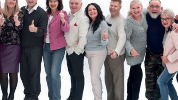 A diverse group of twelve adults stands together, smiling and giving thumbs up. They are dressed in casual clothing, showcasing a sense of joy and celebration. The background is plain white, emphasizing their positive expressions and camaraderie.