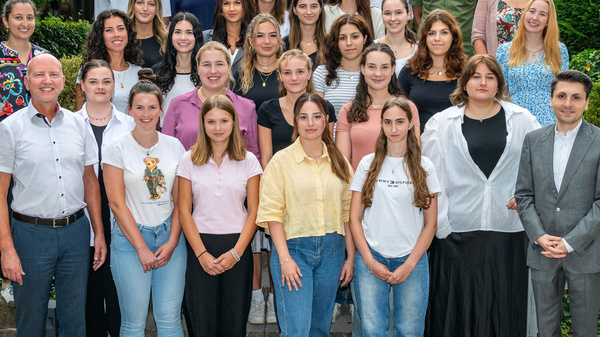 Eine Gruppe von 31 Personen steht draußen auf einer Treppe, umgeben von Bäumen und Sträuchern. Sie sind in verschiedenen Kleidungsstilen gekleidet und lächeln in die Kamera. Im Vordergrund stehen einige Erwachsene, während die anderen Jugendliche und junge Erwachsene sind.