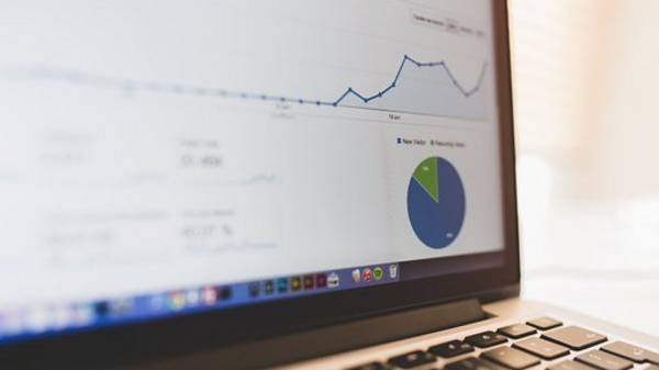 A close-up of a laptop screen displaying data analytics. The screen features a line graph showing fluctuations over time and a pie chart divided into sections, one labeled "New Visitors." This image represents website traffic and performance metrics.