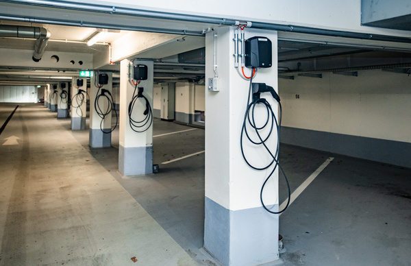 Parkhaus Landratsamt mit E-lademöglichkeiten Ein leerer Parkhausbereich mit mehreren Säulen, an denen Ladestationen für Elektrofahrzeuge installiert sind. Die Kabel sind ordentlich um die Säulen gewickelt, während die Parkplätze deutlich erkennbar sind. Die Wände sind in hellen Farben gehalten.