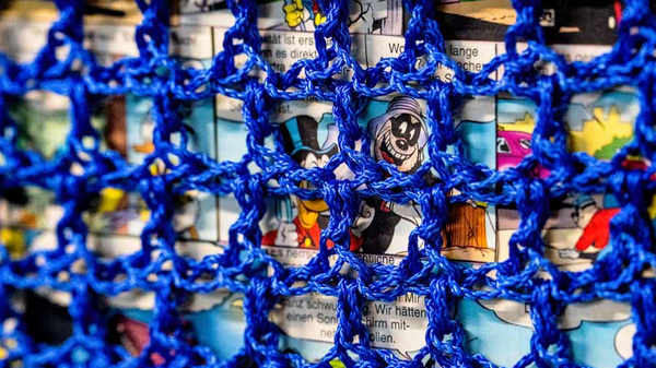 Ein blauer Netzstoff verdeckt bunte Comic-Illustrationen. Die Zeichnungen zeigen Figuren und Szenen aus bekannten Comics. Das Netz gibt dem Bild eine strukturierte Textur und lässt nur Teile der Comics durchscheinen.