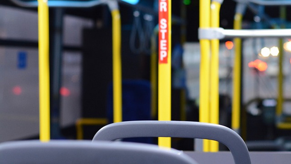 Interior of an empty bus featuring yellow support poles, blue upholstered seats, and dim lighting. The view focuses on the seats with a blurry background of the bus's interior and illuminated signage, suggesting a quiet, waiting atmosphere.