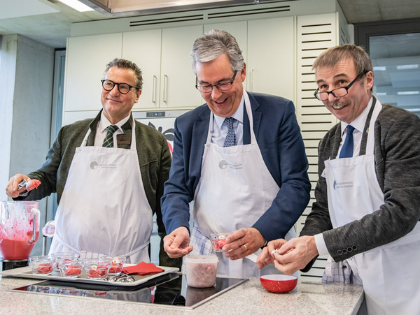 13.03.2023 - Mit Minister Peter Hauk (li.) & Abgeordneter Konrad Epple (re.) bei den Ernährungstagen Drei Männer in Küchenschürzen stehen an einem Kochfeld. Sie bereiten gemeinsam ein Gericht zu, indem sie Zutaten in Gläser füllen. Die Atmosphäre ist freundlich und kooperativ, während sie lächeln und miteinander interagieren.