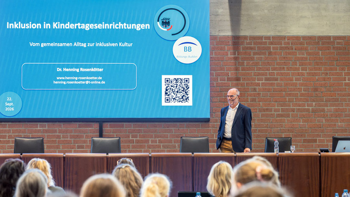 Dr. Henning Rosenkötter steht vor am Pult hinter ihm ist die Präsentation zu Inklusion an Kindertageseinrichtungen zu sehen
