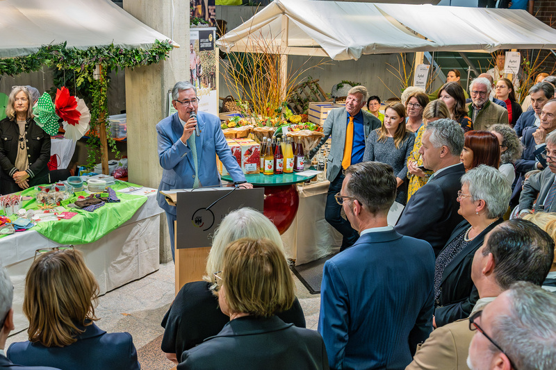 Landrat Dietmar Allgaier steht hinter einem Rednerpult mit Mikrophon in der Hand und begrüßt die umstehenden Menschen