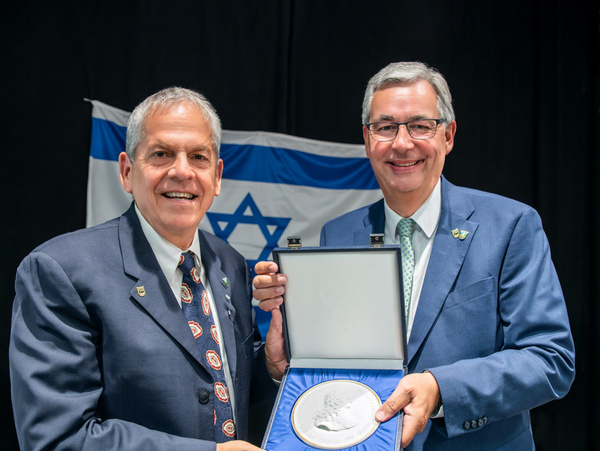 Chairman Giora Salz aus dem Oberen Galiläa wird verabschiedet und erhält Verdienstmedaille Zwei Männer stehen zusammen und halten eine große Medaille in einer Schatulle. Einer der Männer lächelt, während der andere die Medaille zeigt. Im Hintergrund ist eine Flagge mit dem Davidstern sichtbar.