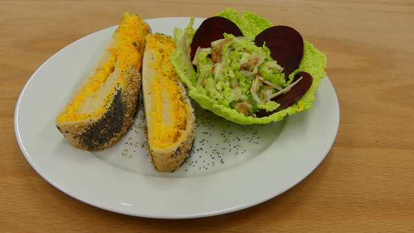 A plate contains two slices of poppy seed bread filled with bright yellow ingredients, alongside a colorful salad made of green lettuce and red beets. The dish presents a mixture of textures and contrasts in color, emphasizing a fresh, healthy meal.