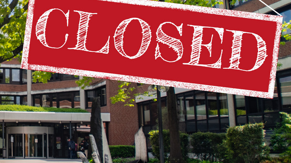 Ein Gebäude mit einem Schild, das "CLOSED" (geschlossen) anzeigt, hängt über dem Eingang. Die Umgebung besteht aus einem grünen Garten mit Bäumen und Sträuchern. Es ist sonnig und der Bereich wirkt ruhig.