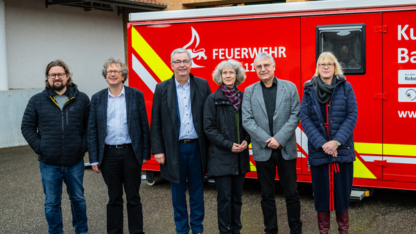 Sechs Personen stehen vor einem Einsatzfahrzeug der Feuerwehr mit der Aufschrift "Kulturgutschutz Baden-Württemberg". Sie wirken freundlich und professionell, bereit zur Zusammenarbeit im Bereich des Kulturgutschutzes. Das Fahrzeug betont die Bedeutung des Schutzes von Kulturgütern in der Region.