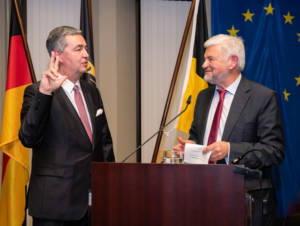 17.01.2020 - Amtseinsetzung Dietmar Allgaier durch Regierungspräsident Wolfgang Reimer Ein Mann legt den Eid ab, während ein anderer ihn dabei beobachtet. Beide stehen an einem Rednerpult vor Flaggen Deutschlands und der EU. Der erste Mann trägt einen Anzug und hat die rechte Hand vorgestreckt, während der zweite Mann lächelt und Unterlagen in der Hand hält.