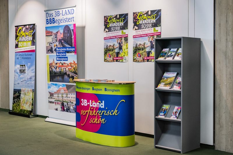 Ein Messestand des 3B-Lands mit einem Empfangstresen und einem Bücherregal. An der Wand hängen Plakate, die für Wandertouren in der Region werben. Der Tresen trägt den Schriftzug „3B-Land verführerisch schön“. Flyer liegen auf dem Tresen bereit.