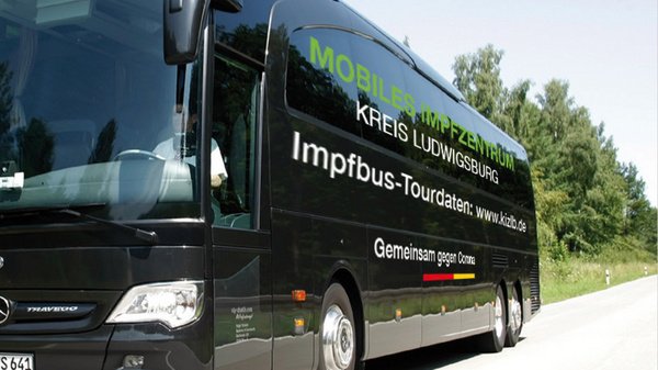 Autocar noir en mouvement sur une route, portant des inscriptions sur sa carrosserie concernant un service de vaccination. Le texte mentionne "Mobilité" et "Impfbus", indiquant qu'il s'agit d'un bus dédié aux vaccinations. L'environnement autour est naturel, avec des arbres en arrière-plan.