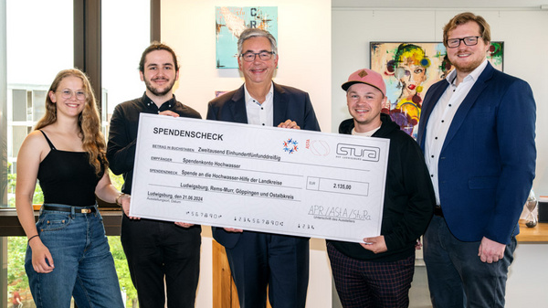 Eine Gruppe von fünf Personen steht in einem hellen Raum und hält einen großen Scheck in der Hand. Der Scheck ist für eine Spende über 2.510 Euro und richtet sich an die „Hilfe für Menschen mit Behinderungen“. Die Personen lächeln und schauen in die Kamera.