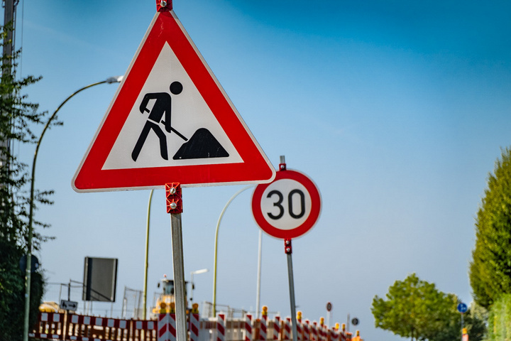 Das Bild zeigt ein Verkehrsschild mit der Warnung vor Baustellen, dargestellt durch eine Person, die mit einer Schaufel arbeitet. Neben dem Baustellenschild ist ein weiteres Schild mit einer Geschwindigkeitsbegrenzung von 30 km/h zu sehen.