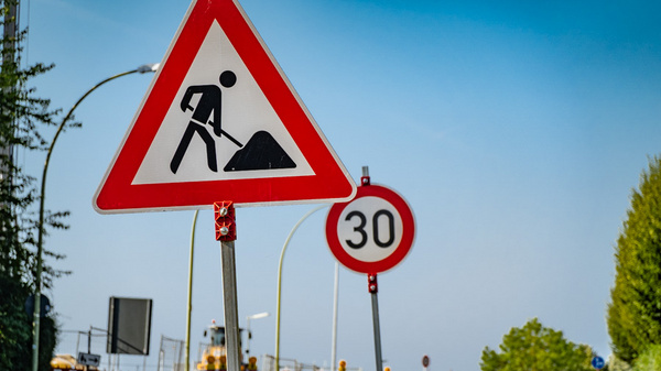 Das Bild zeigt ein Verkehrsschild mit der Warnung vor Baustellen, dargestellt durch eine Person, die mit einer Schaufel arbeitet. Neben dem Baustellenschild ist ein weiteres Schild mit einer Geschwindigkeitsbegrenzung von 30 km/h zu sehen.
