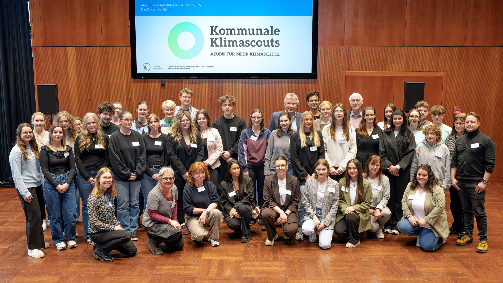 Un gruppo di circa 40 persone, tirocinanti e mentori, si ritrovano insieme per una foto di gruppo. Sullo sfondo è visibile una diapositiva di presentazione del progetto "Municipal Climate Scouts".