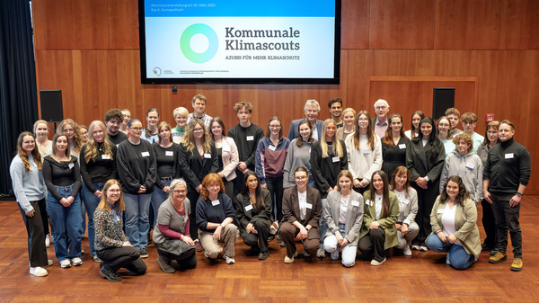 Un gruppo di circa 40 persone, tirocinanti e mentori, si ritrovano insieme per una foto di gruppo. Sullo sfondo è visibile una diapositiva di presentazione del progetto "Municipal Climate Scouts".