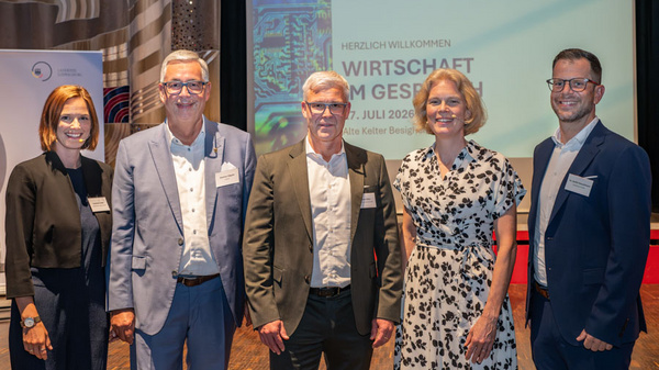 Eine Gruppe von fünf Personen steht lächelnd vor einem Banner mit dem Titel „Wirtschaft im Gespräch“. Sie sind in formeller Kleidung und stehen auf einer Bühne, die für eine Veranstaltung vorbereitet ist.
