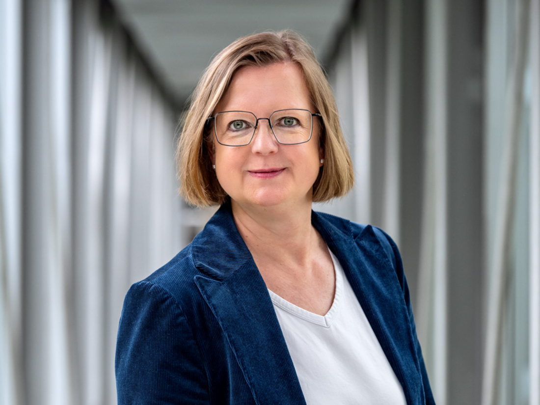 Dott.ssa Carolin Meier Porträt einer Frau mit kurzen, blonden Haaren, die eine Brille trägt. Sie steht in einem modernen, hellen Flur mit vertikalen Elementen im Hintergrund und blickt freundlich in die Kamera. Sie trägt einen blauen Blazer über einem weißen Oberteil.