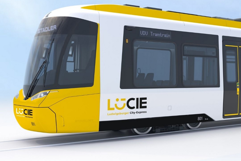 Ein moderner Straßenbahnwagen in Gelb und Weiß mit der Aufschrift „LüCIE – City Express“. Die Front ist aerodynamisch gestaltet, und die Seitenfenster sind groß, um den Passagieren Sicht zu bieten. Die Bahn steht auf Schienen vor einem hellen, wolkenlosen Hintergrund.