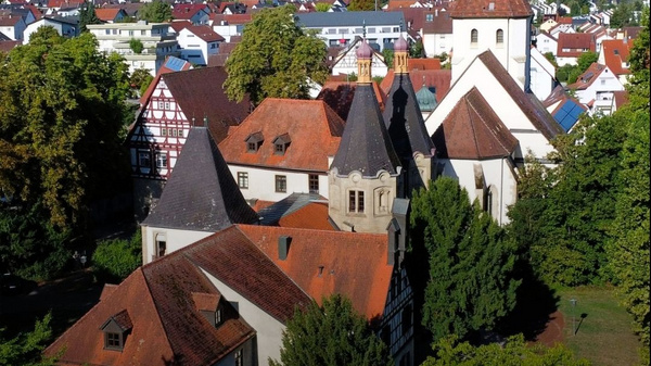 Luftaufnahme eines historischen Gebäudes in Hemmingen, umgeben von Bäumen und Wohnhäusern. Im Vordergrund sind ein Rathaus und ein Kirchturm sichtbar. Darüber steht der Text „Hemmingen ENTDECKE UNSERE REGION“. (Text KI generiert)
