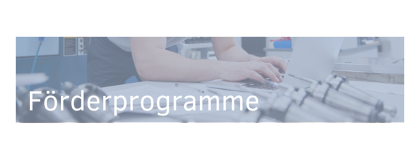 A person typing on a laptop amid various tools and equipment, with the text "Förderprogramme" prominently displayed. The image suggests a focus on funding programs related to technology or manufacturing.