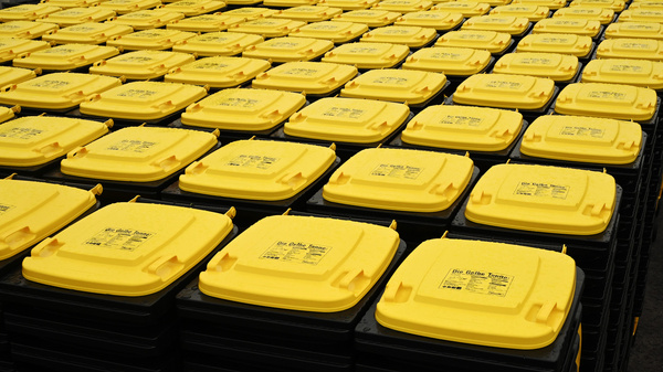 L'image montre un grand nombre de conteneurs en plastique noir avec des couvercles jaunes, disposés en rangées serrées. Chaque conteneur est étiqueté avec des informations. L'ensemble crée une impression d'organisation et de stockage.