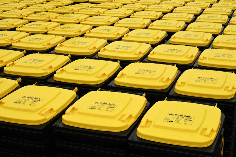 Die Abbildung zeigt eine große Menge von schwarzen Mülltonnen mit gelben Deckeln, die ordentlich in Reihen angeordnet sind. Die Tonnen scheinen für die Müllentsorgung oder das Recycling bestimmt zu sein. (Text KI generiert)