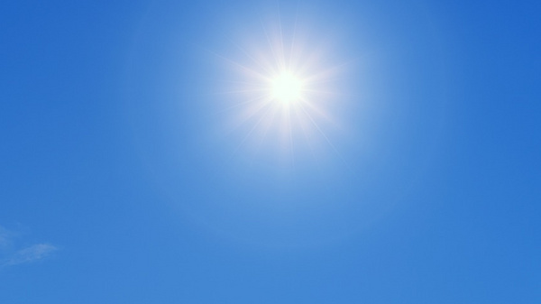 Ein klarer, blauer Himmel mit einer strahlenden Sonne. Die Sonne erscheint hell und bringt ein Gefühl von Wärme und Taglicht. Es gibt nur wenige Wolken im Hintergrund.
