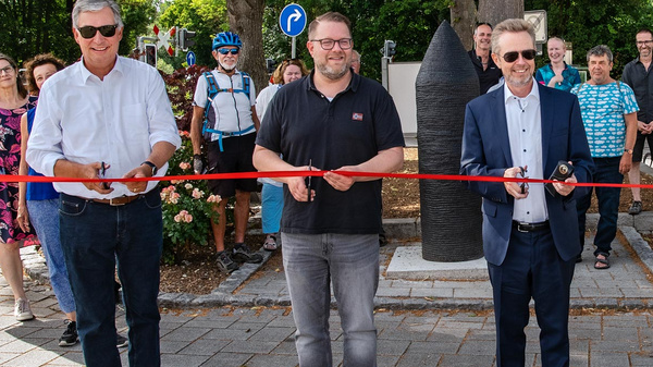 Die Bilder zeigen eine Eröffnungszeremonie mit mehreren Personen, die zusammen ein rotes Band durchschneiden. Im Hintergrund sind Bäume und eine Skulptur zu sehen. Die Anwesenden versammeln sich zur Feier des Anlasses, während einige Radfahrer im Hintergrund stehen.