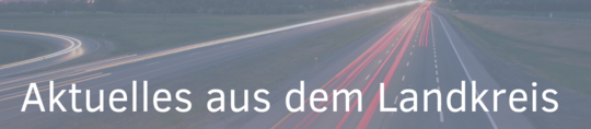 Eine Straße mit Fahrzeuglichtern im Dunkeln, die Bewegungsrichtung sichtbar macht. Oberhalb des Bildes steht in großer Schrift: "Aktuelles aus dem Landkreis".