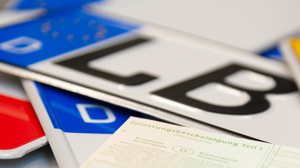 The image features various vehicle license plates, prominently displaying the letters "LB" and the letter "D," along with a vehicle registration document in a green color. The documents and plates are arranged closely together, emphasizing their importance in vehicle identification.