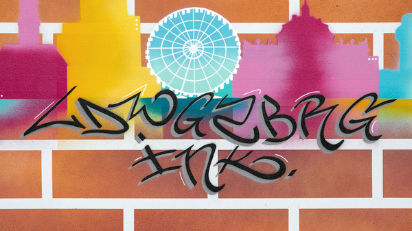 A colorful graffiti mural featuring a city skyline against a brick background. The skyline includes notable structures in various shades of purple, yellow, and blue, with a large ferris wheel at the center. The text "ADWGRBBK INK." is artistically incorporated into the design.