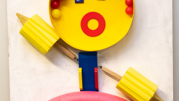 A colorful, abstract figure resembling a weightlifter is depicted. The head is a yellow circle with colorful dots for eyes and hair, while a red circular body features various colored buttons. The figure holds a barbell, emphasizing a playful, creative design suitable for a children's environment.