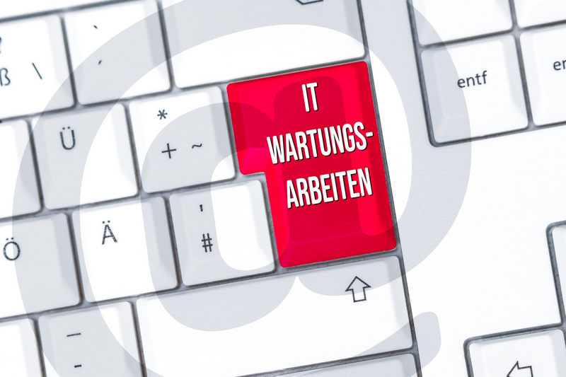 Ein Computer-Tastatur mit einer hervorgehobenen roten Taste, auf der "IT WARTUNGS-ARBEITEN" steht. Der Hintergrund enthält ein grafisches Element, das eine Art Kreis oder Welle darstellt. (Text KI generiert)