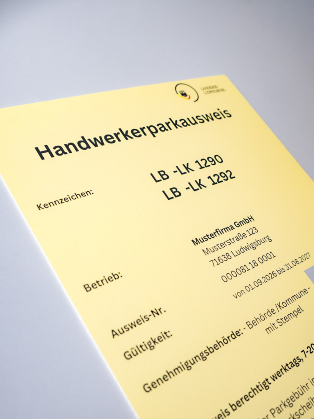 Ein gelber Handwerkerparkausweis mit der Aufschrift "Handwerkerparkausweis" und Kennzeichen "LB -LK 1290" sowie "LB -LK 1292". Darunter steht der Name einer Musterfirma und weitere Details wie Adresse, Ausweis-Nr., Gültigkeit und die Genehmigungsbehörde. (Text KI generiert)
