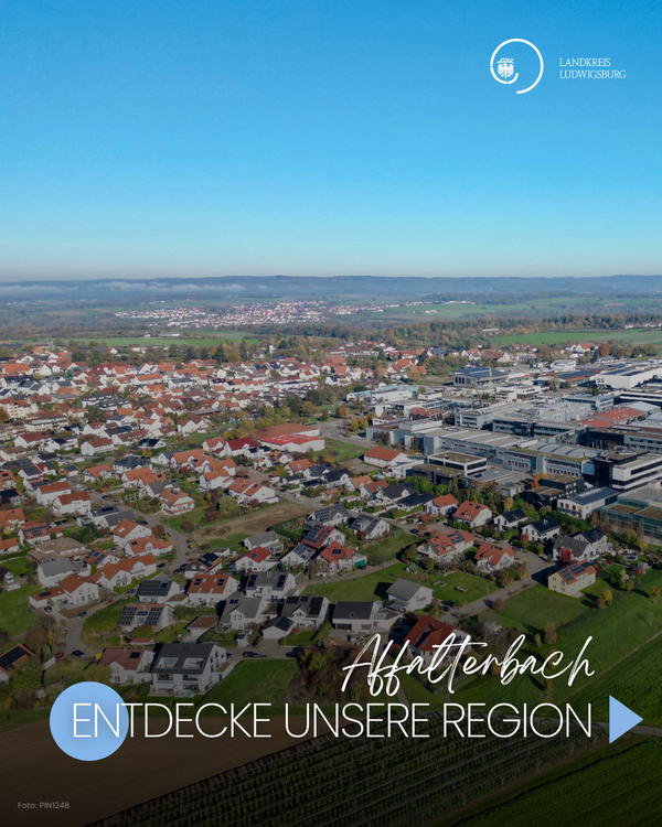 Eine Luftaufnahme von Affalterbach zeigt die umliegenden Wohngebiete und die Landschaft. Im Vordergrund sind Wohnhäuser zu sehen, während im Hintergrund industrielle Gebäude und die grüne Umgebung sichtbar sind. Der Text "Entdecke unsere Region" lädt ein, mehr über die Gegend zu erfahren.