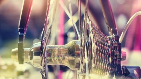 Close-up of a bicycle wheel, focusing on the hub and cassette. The metal components reflect light in various hues, showcasing intricate details of the gears. The background is softly blurred, emphasizing the wheel's mechanics against a colorful backdrop.