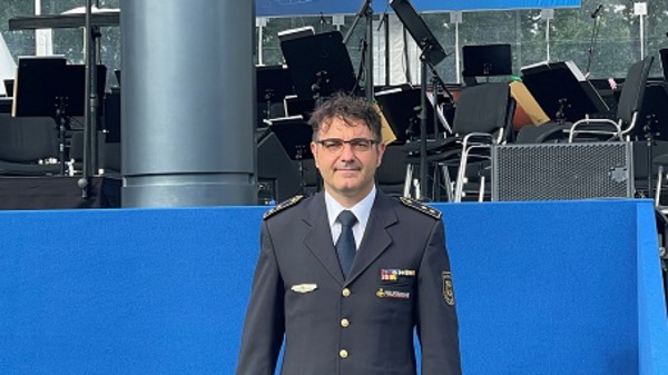 Un homme en uniforme de police se tient sur scène, devant un podium et un panneau bleu. Le panneau, en allemand, agradeci à ceux qui ont aidé durant la pandémie de Corona. Des chaises pour un orchestre sont visibles en arrière-plan.