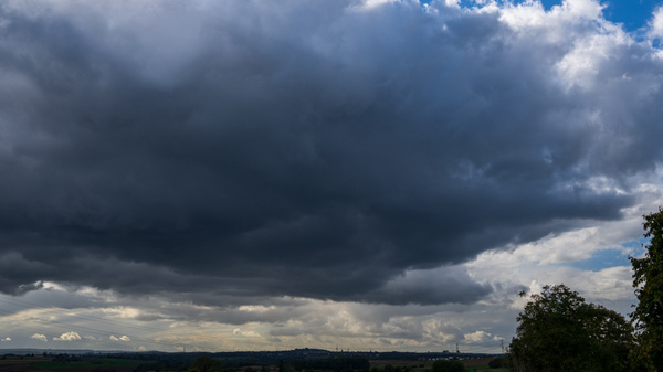 Dunkle, bedrohliche Wolken dominieren den Himmel über einer grünen Landschaft, während sich der Himmel auflockert und hellere Farben am Horizont erscheinen. (Text KI generiert)