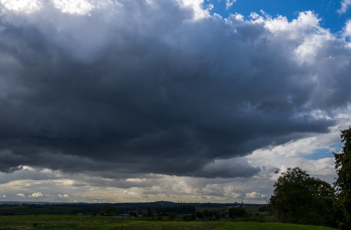 Dunkle, bedrohliche Wolken dominieren den Himmel über einer grünen Landschaft, während sich der Himmel auflockert und hellere Farben am Horizont erscheinen. (Text KI generiert)